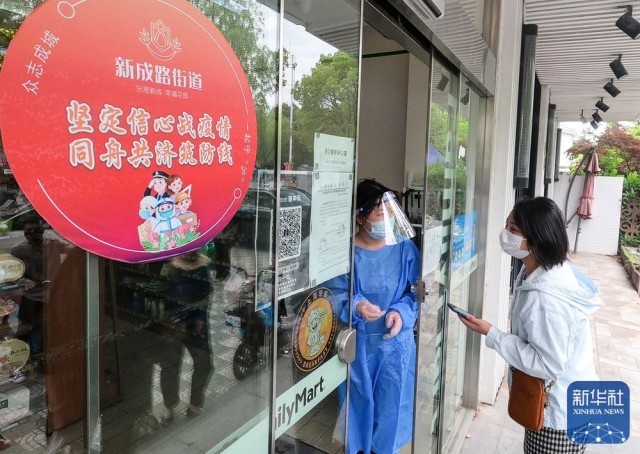 在上海市嘉定区新成路街道，一名顾客（右）在扫码后等待进入便利店（5月9日摄）。该街道经过认定符合防疫规范的经营场所会张贴红色圆形标识。