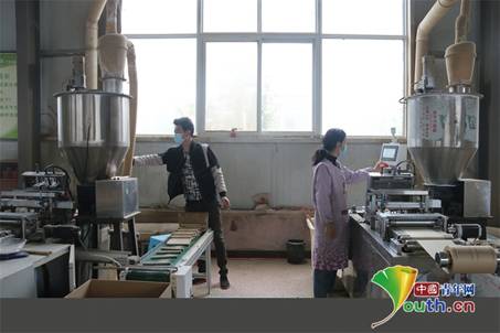 张小兵、谭亚清夫妻俩正在艾制品厂操作全自动艾条加工机械。