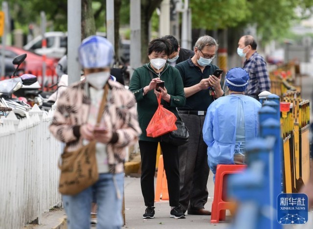 在上海市嘉定区新成路街道一农贸市场门口，买菜的居民向值守工作人员出示核酸检测报告（5月9日摄）。